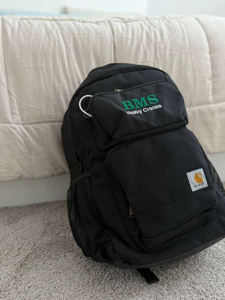 BMS Carhartt Backpack 27L in black with embroidered BMS Heavy Cranes logo, front zip pockets, and side mesh pockets, ideal for daily commuting.