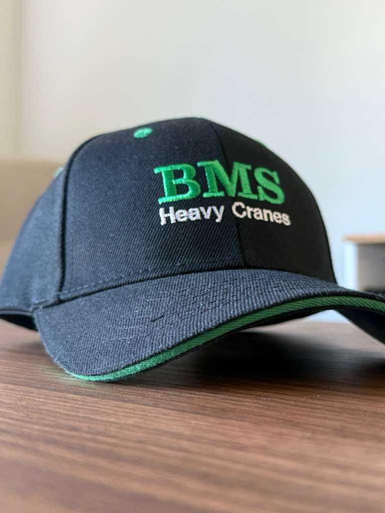Close-up of BMS Black/Green Trucker Hat from Job-Site Series, showing detailed embroidery and green accent stitching on the brim.