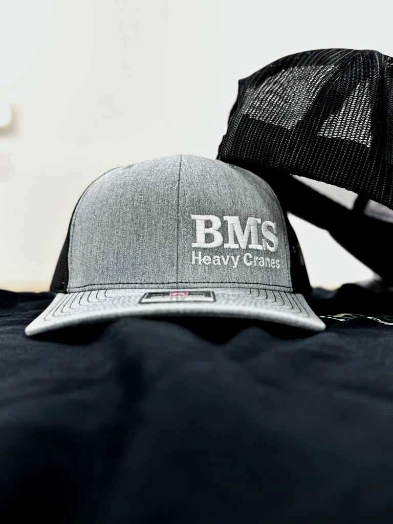 Front view of BMS Black/Grey Trucker Hat with bold embroidered logo and Richardson 112 label, ideal for jobsite wear.