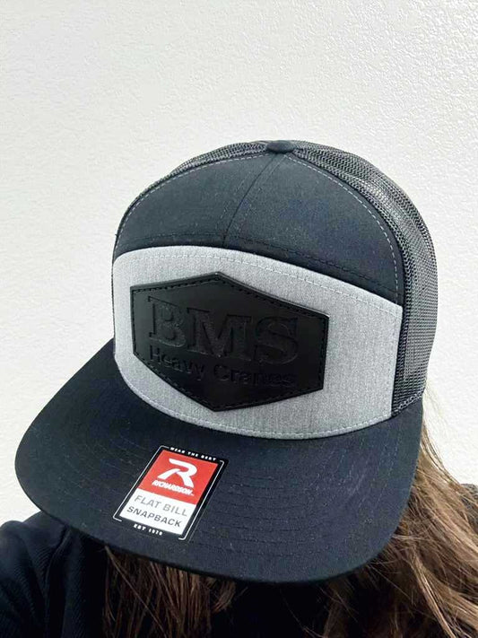 BMS Heavy Cranes Black/Grey Trucker Hat worn on head, showcasing structured front panel and breathable mesh back for workwear comfort.