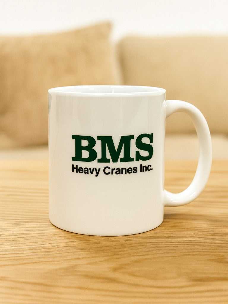 BMS white ceramic mug with bold green BMS Heavy Cranes Inc. logo, ideal for office or jobsite coffee breaks. Durable and stylish workday essential.